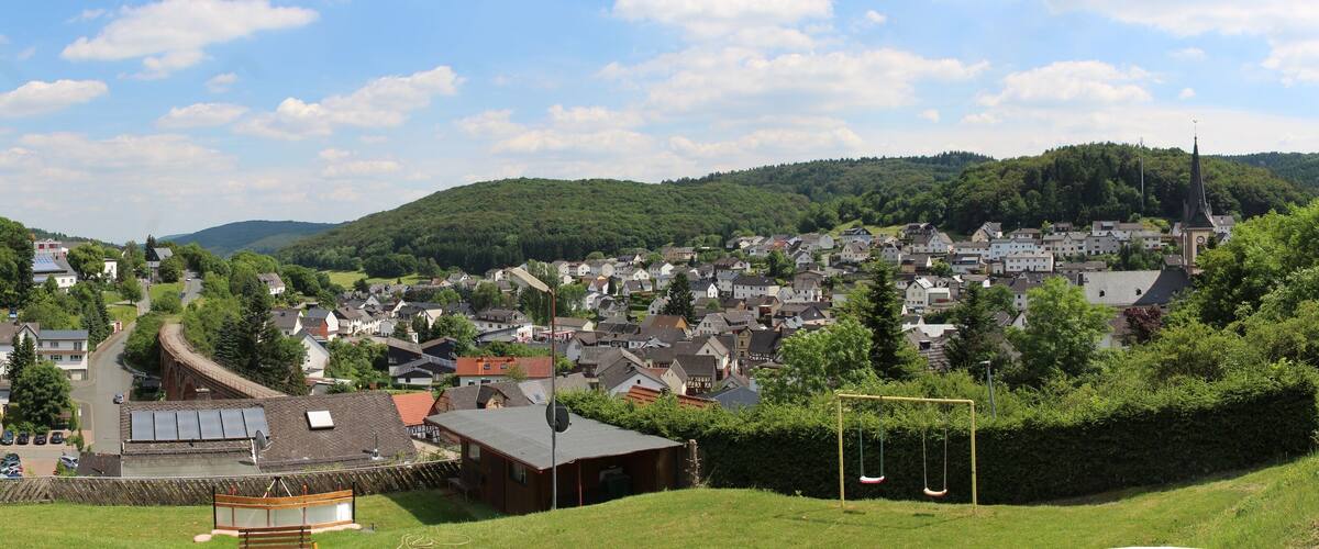 A town nestled in a valley with a river running through it, surrounded by hills and greenery.