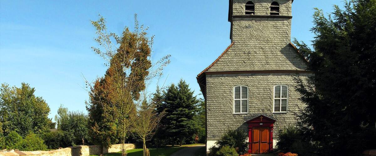 A church with a bell tower, surrounded by trees and a stone wall.
