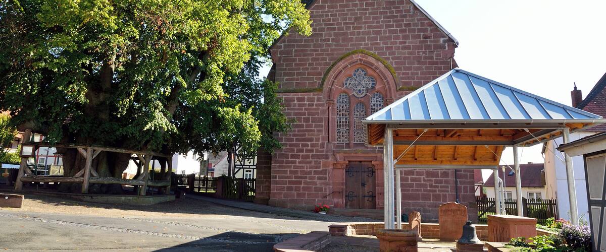 A church with a steeple, a wooden bench, and a gazebo.