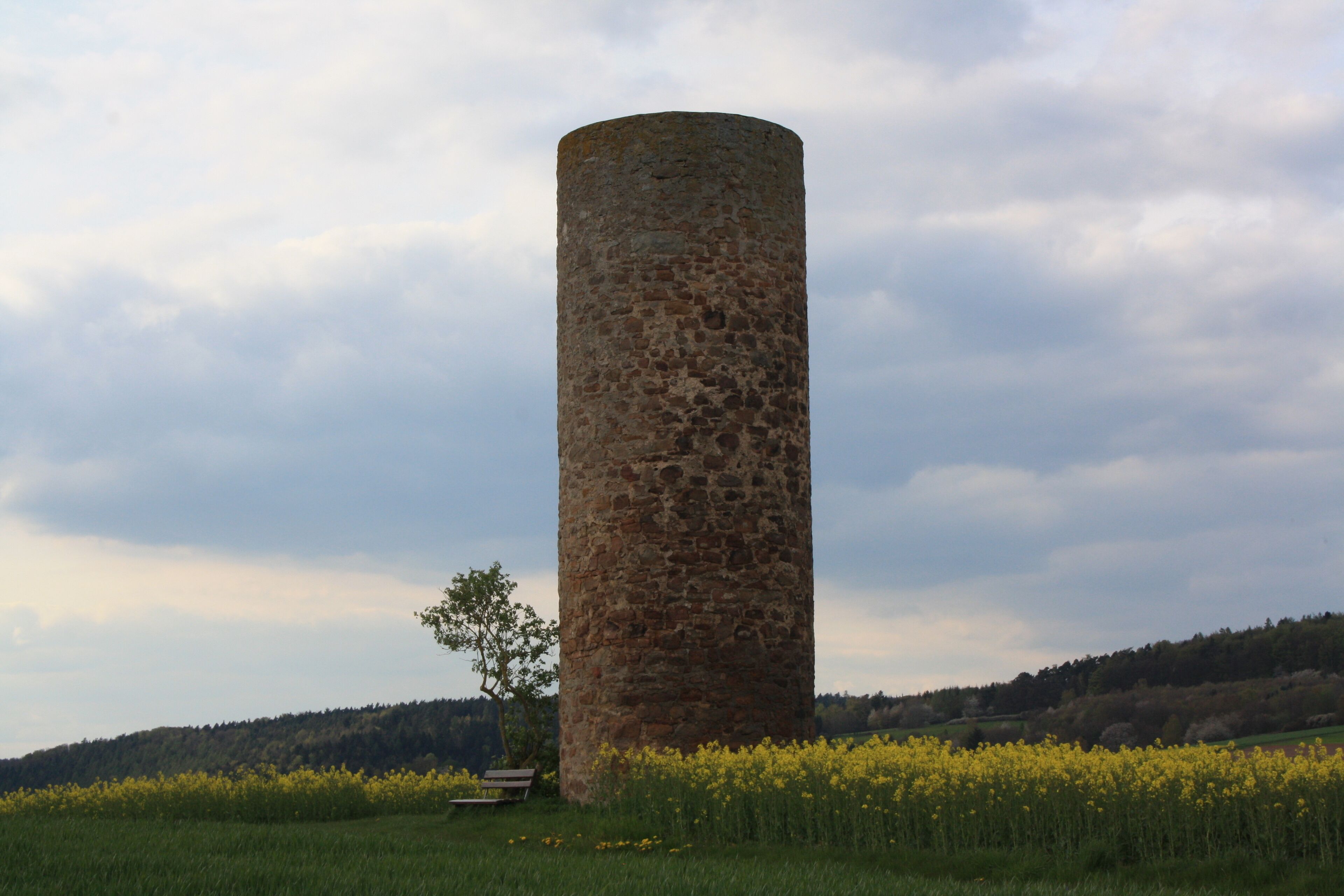 A tall stone tower in a field with yellow flowers and a bench.