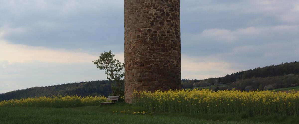A tall stone tower in a field with yellow flowers and a bench.