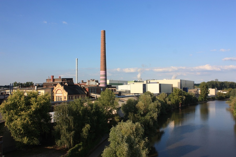 Un río con edificios industriales y una chimenea alta.