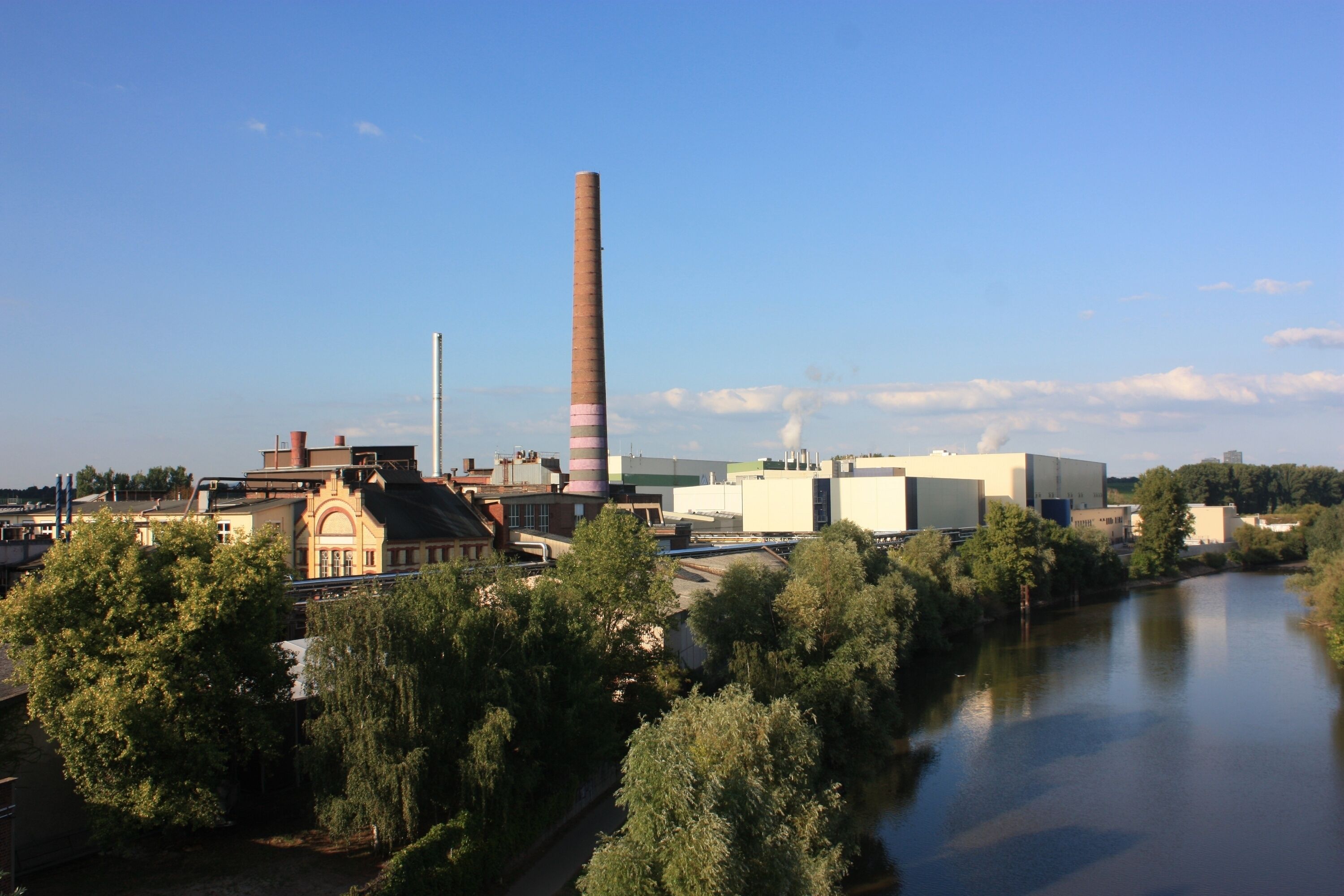 A river with industrial buildings and a tall chimney.