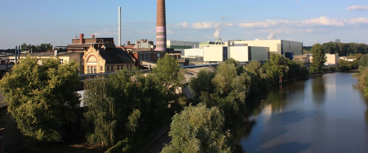A river with industrial buildings and a tall chimney.