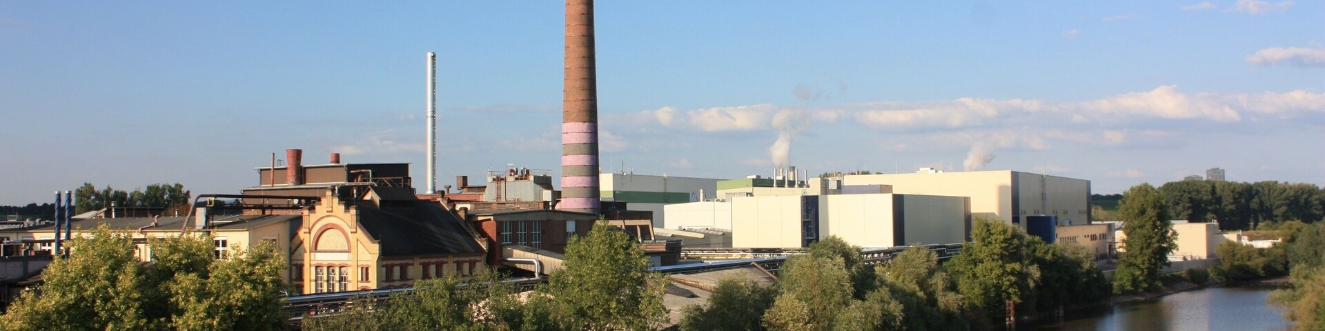 A river with industrial buildings and a tall chimney.