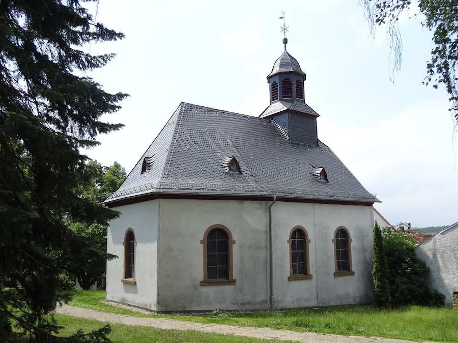 Une église dotée d’un toit à forte pente, d’une petite tour surmontée d’une girouette et de fenêtres en arc.