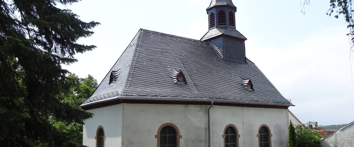 A church with a steeply pitched roof, a small tower with a weather vane, and arched windows.