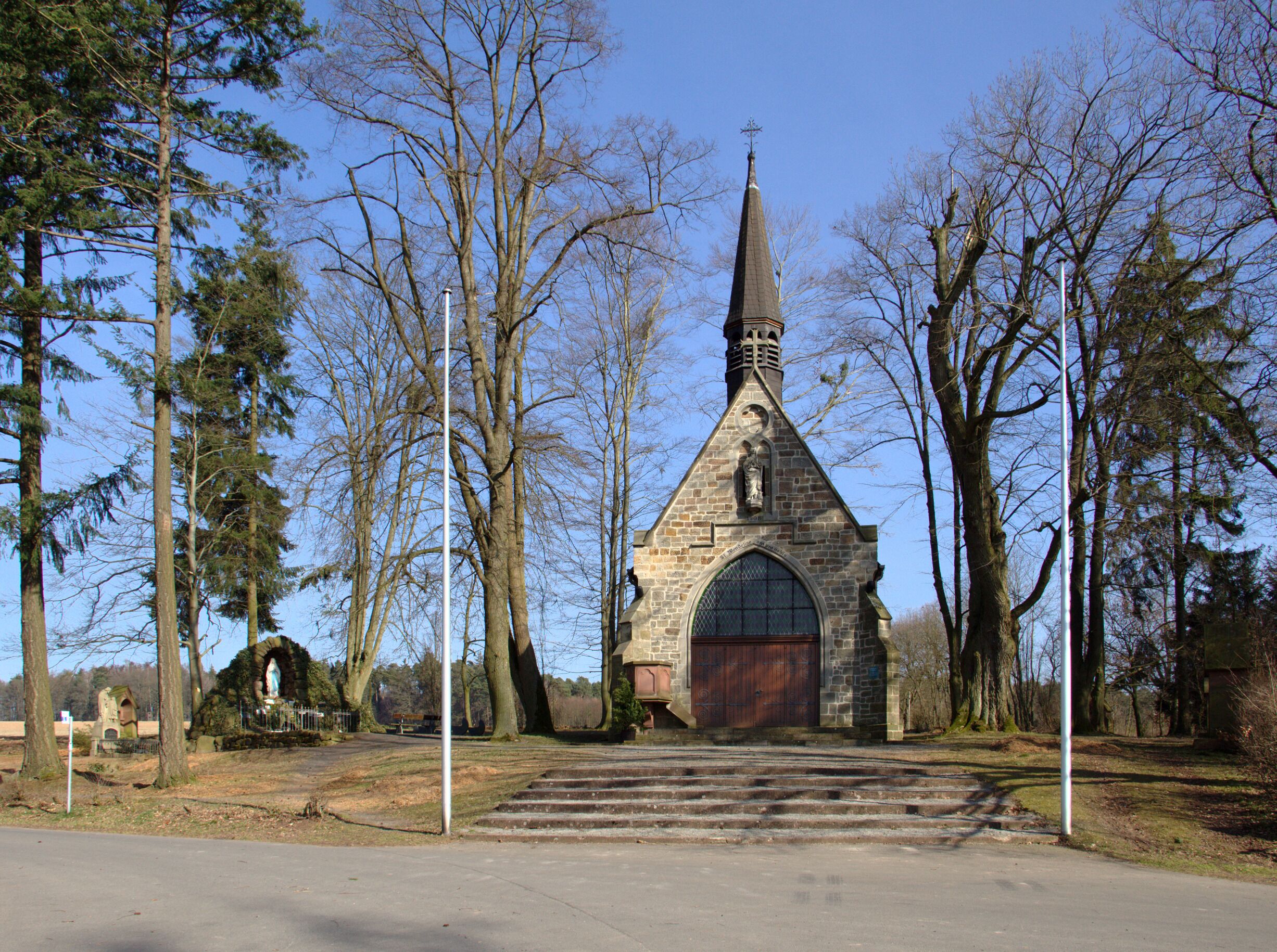 A stone church with a pointed steeple, surrounded by trees.