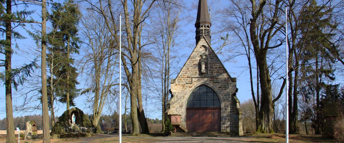 A stone church with a pointed steeple, surrounded by trees.