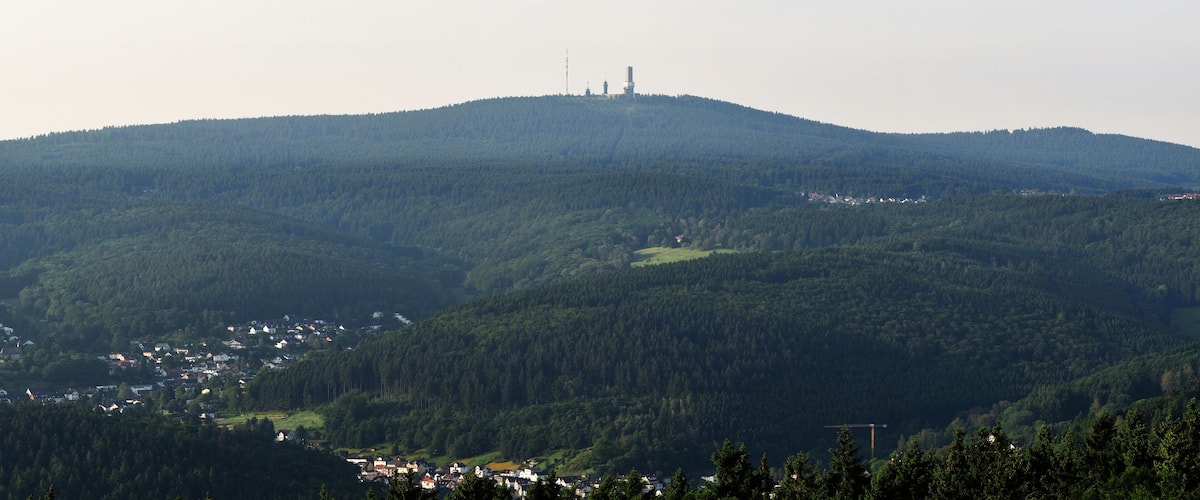 A mountainous landscape with a village at the base, dense forest, and a tower on the hill.