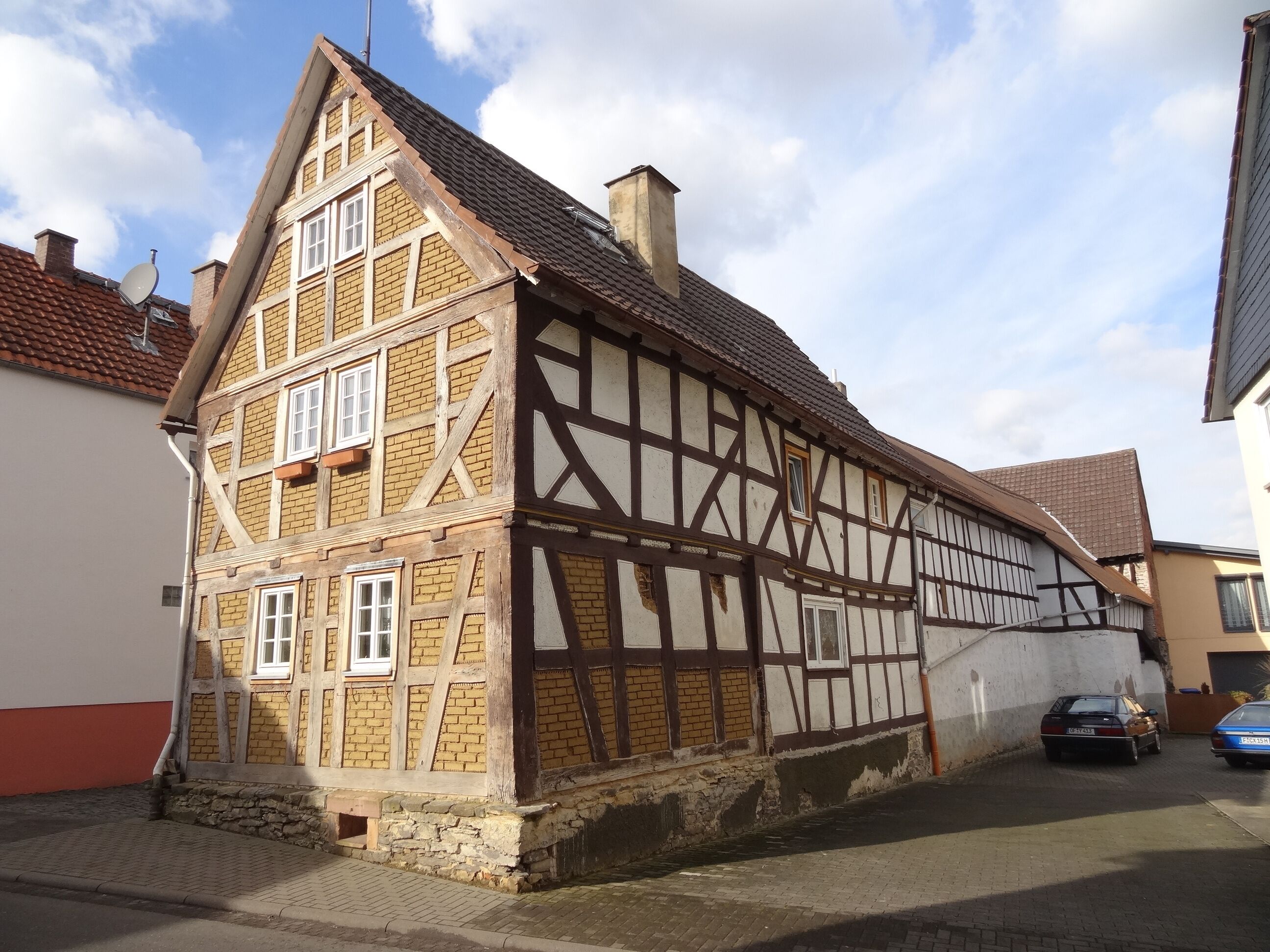 A traditional half-timbered house with a steeply pitched roof, a satellite dish, and a stone foundation.