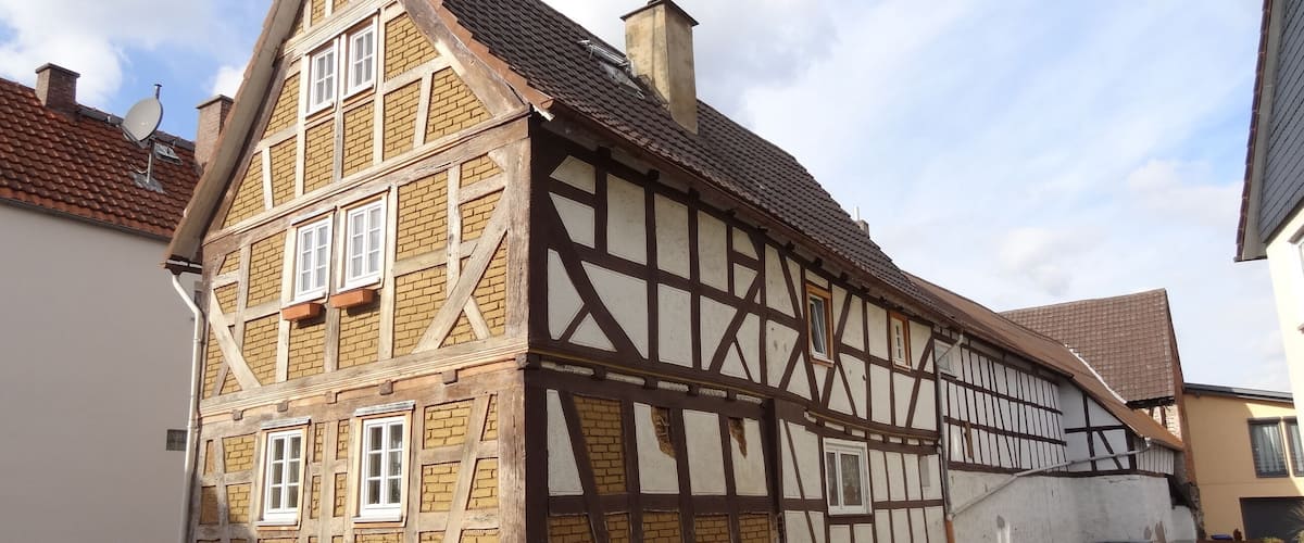 A traditional half-timbered house with a steeply pitched roof, a satellite dish, and a stone foundation.