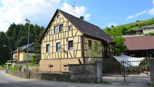 A traditional half-timbered house with a sloped roof, surrounded by a stone wall and a metal fence.