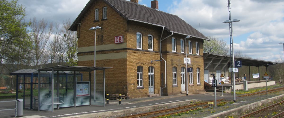 A train station with a brick building, a shelter, and multiple tracks.