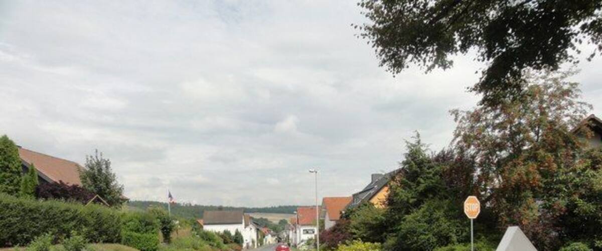 A quiet suburban street with houses, a stop sign, and a bench.