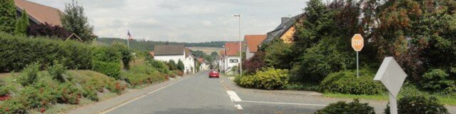 A quiet suburban street with houses, a stop sign, and a bench.