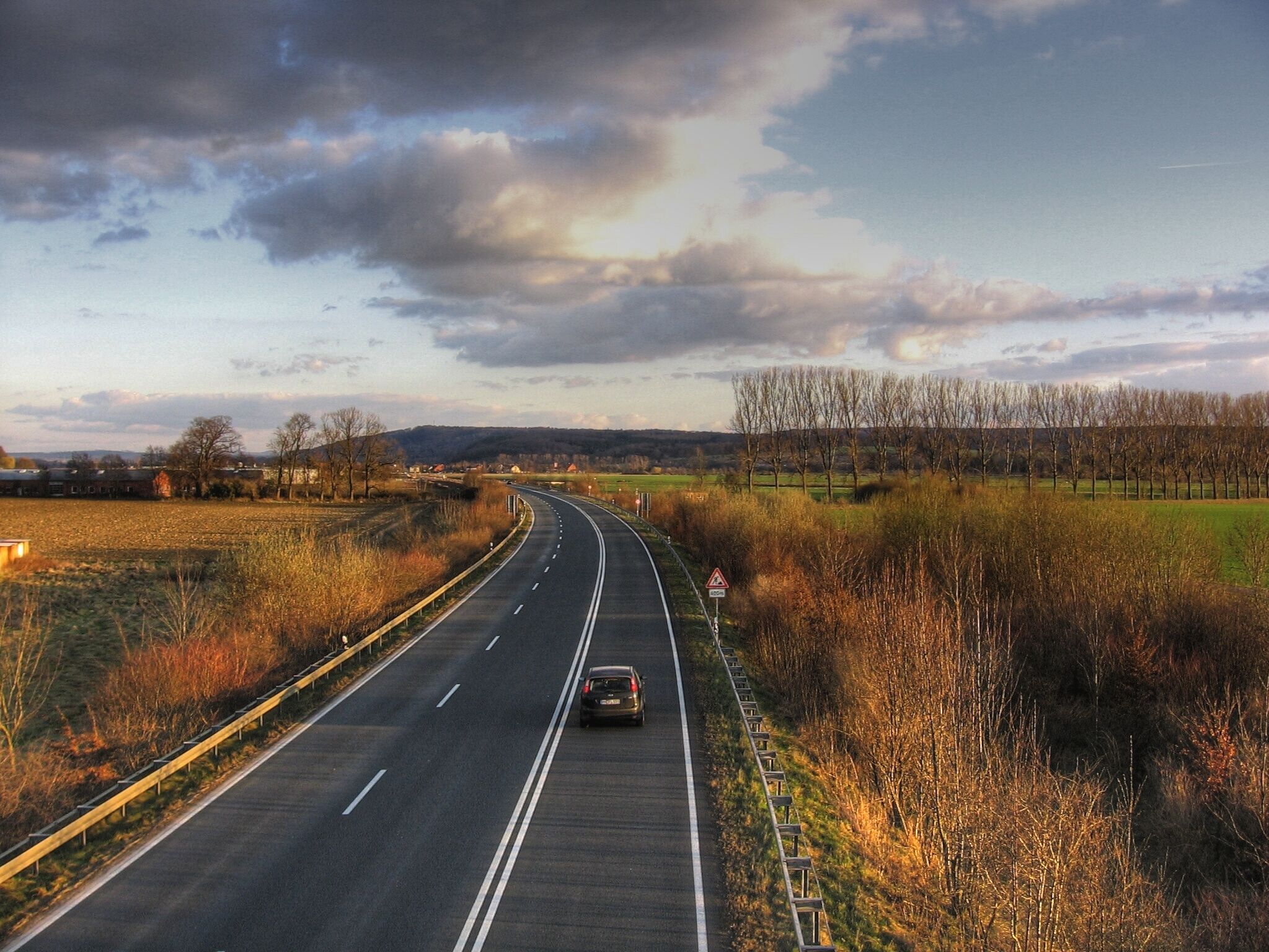 A highway curving through a rural landscape with fields and trees.