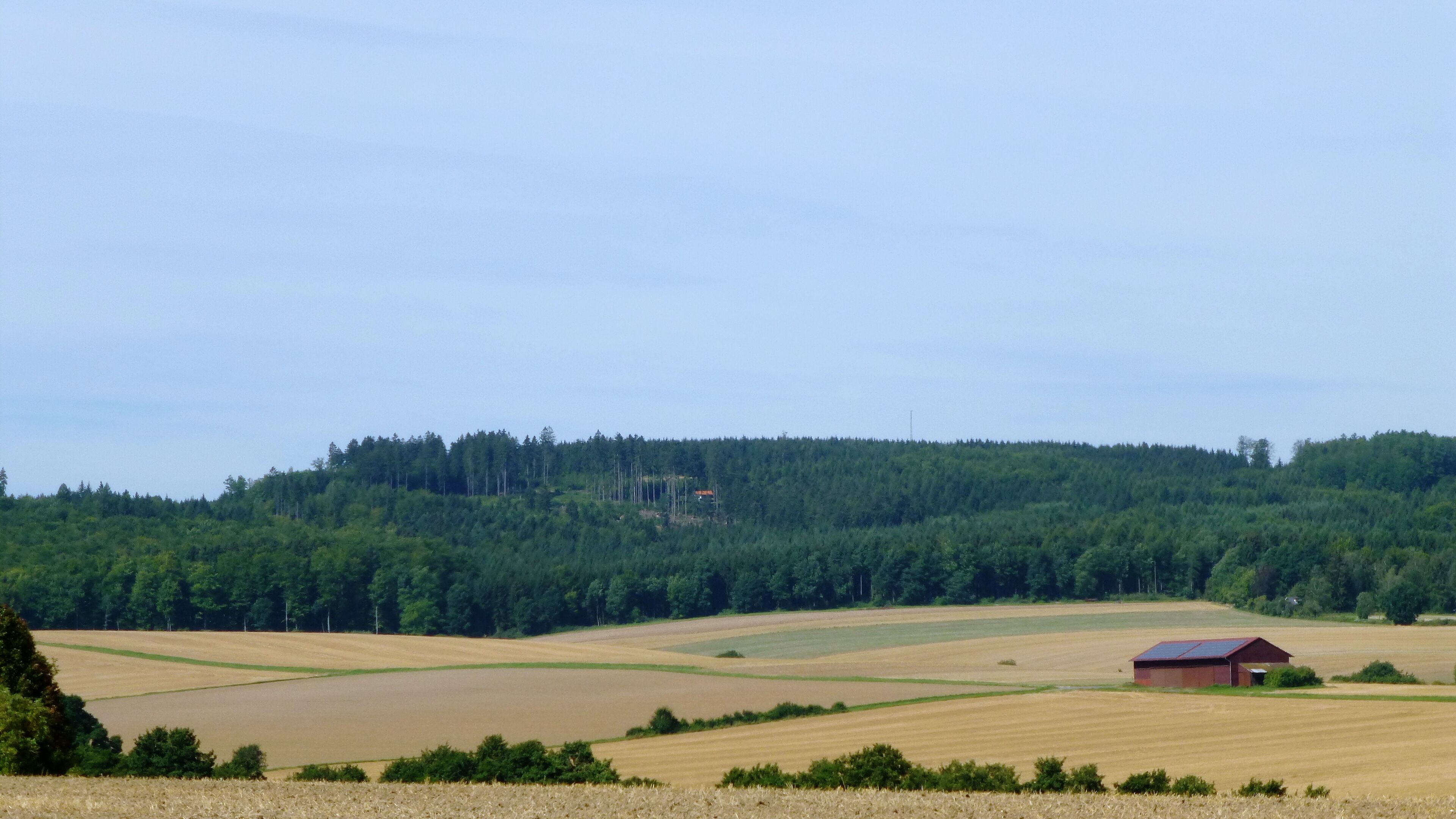A rural landscape with a forested hill, agricultural fields, and a small red barn.