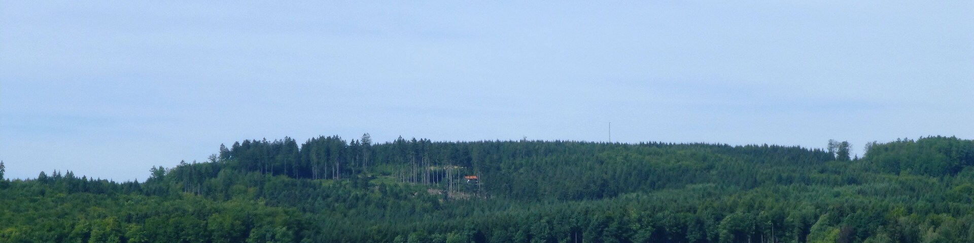 A rural landscape with a forested hill, agricultural fields, and a small red barn.