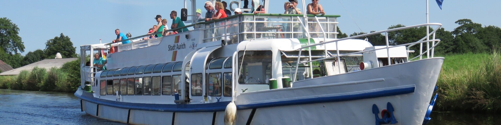 A riverboat with passengers, a flag, and a calm waterway.