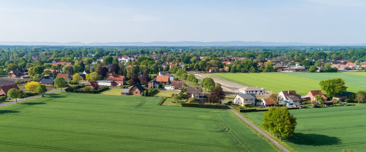 A rural landscape with houses, green fields, and distant mountains.