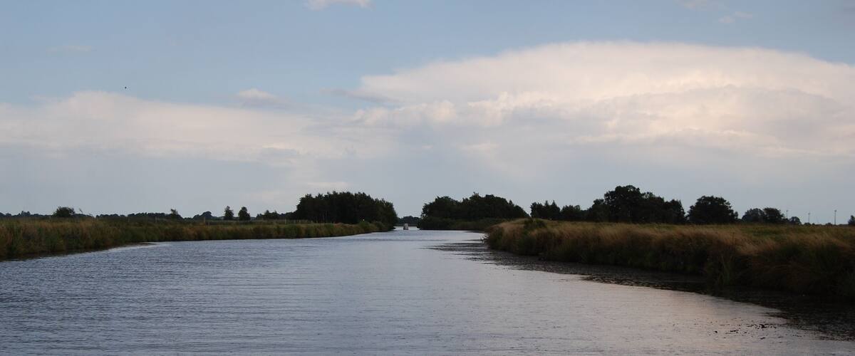 A river winding through a landscape with grassy banks and trees in the distance.