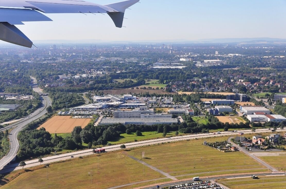 An aerial view of a city with a large industrial area, highways, and surrounding greenery.
