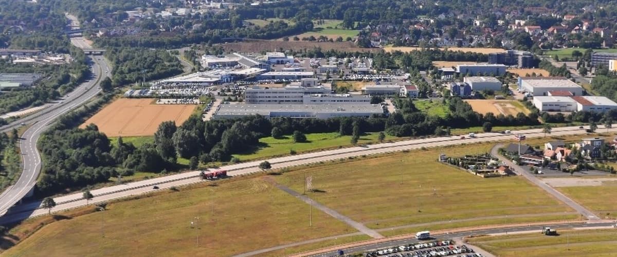 An aerial view of a city with a large industrial area, highways, and surrounding greenery.