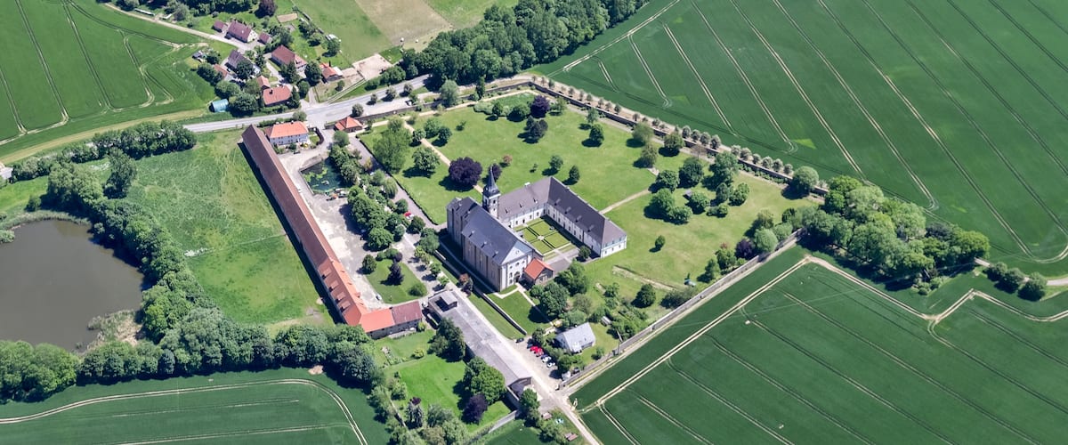 Eine Luftaufnahme eines weitläufigen Anwesens mit ausgedehnten Grünflächen, einem zentralen Gebäudekomplex und einem See.