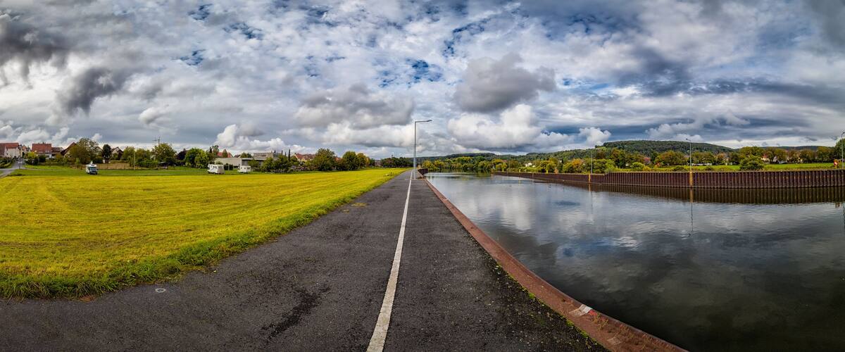 A canal with a grassy field on one side and a road leading to a town.