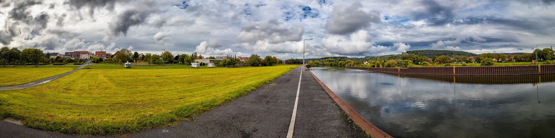 A canal with a grassy field on one side and a road leading to a town.
