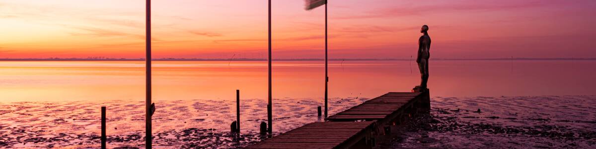 A sunset over a calm sea with a wooden pier and flags.