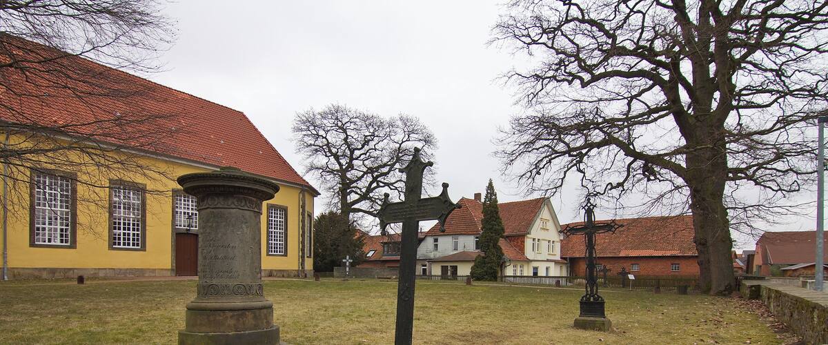 A cemetery with a yellow building, stone crosses, and a large tree.