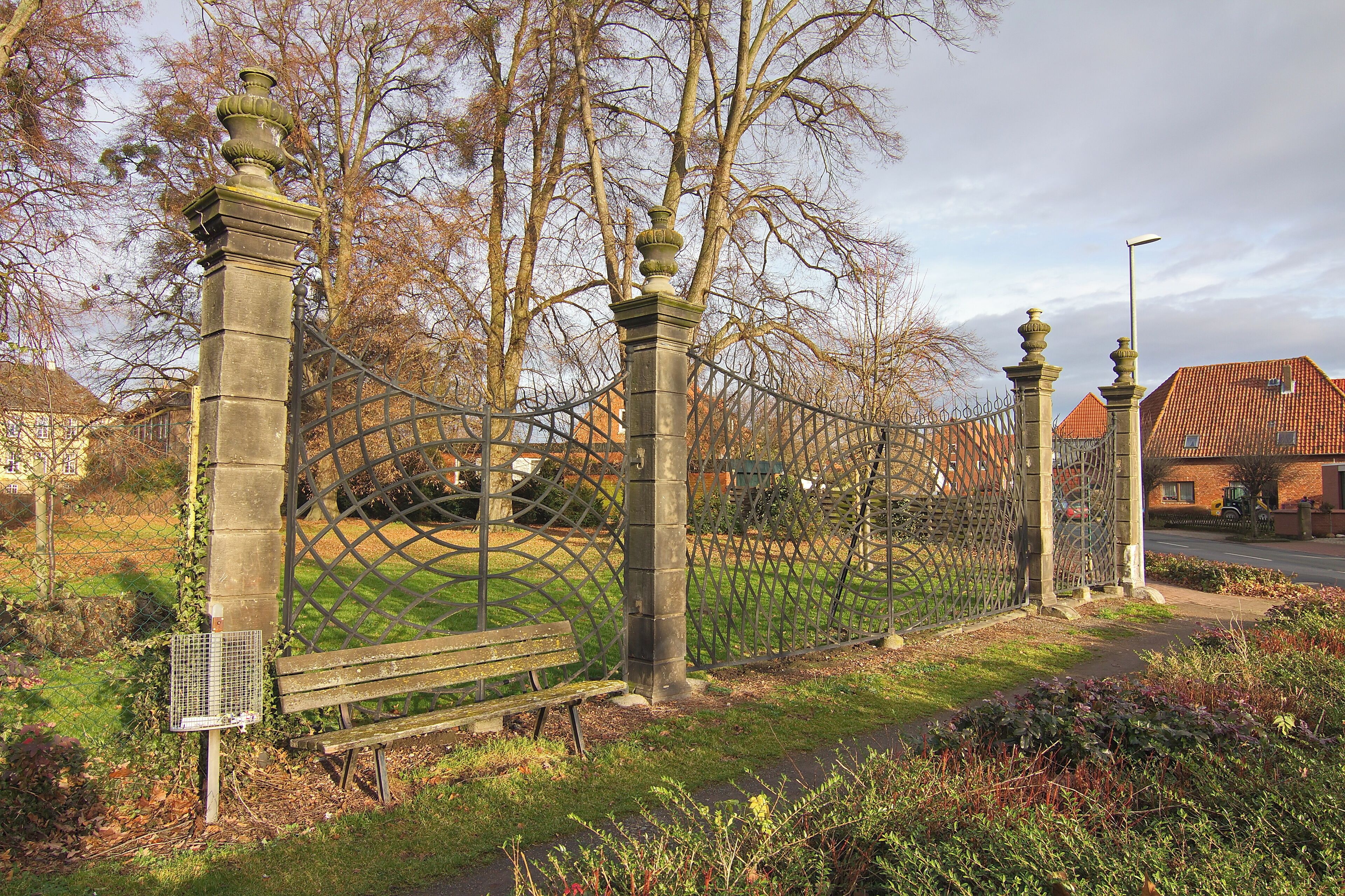 A wrought iron fence, a bench, and a building with a red roof.
