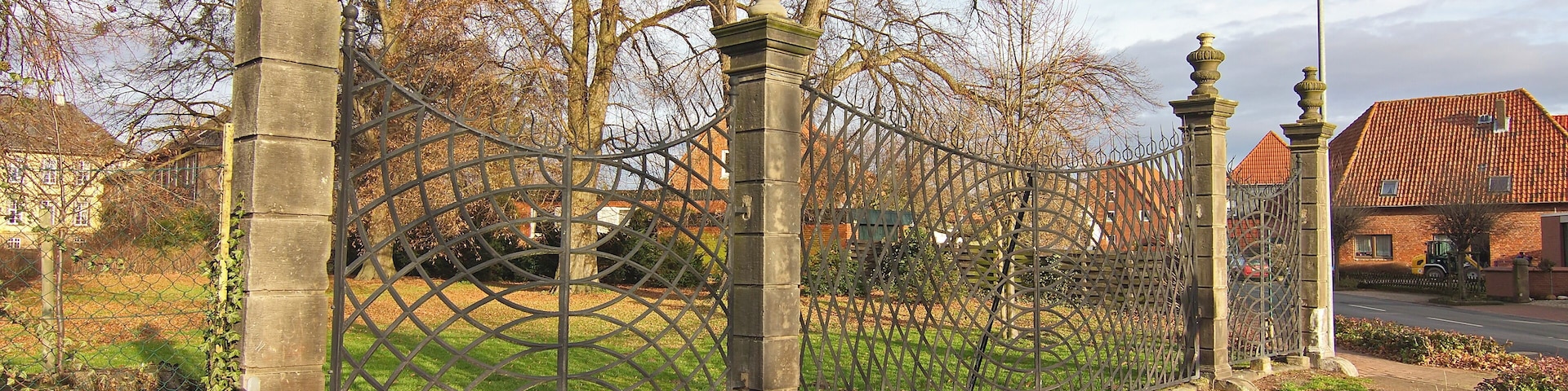 A wrought iron fence, a bench, and a building with a red roof.