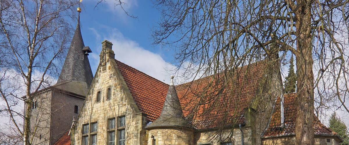 A historic stone building with a red-tiled roof and multiple spires.