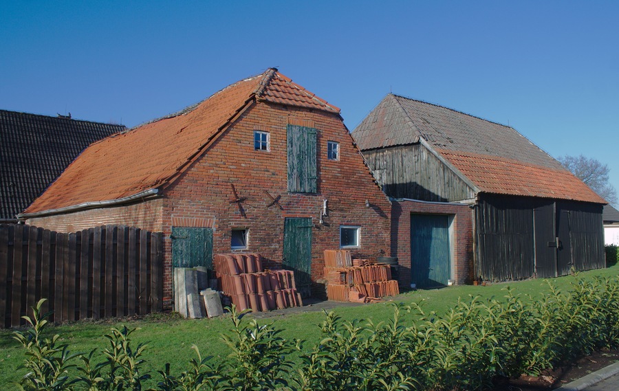 Ein Backsteinhaus mit rotem Dach, ein hölzerner Schuppen und ein Holenzaun.