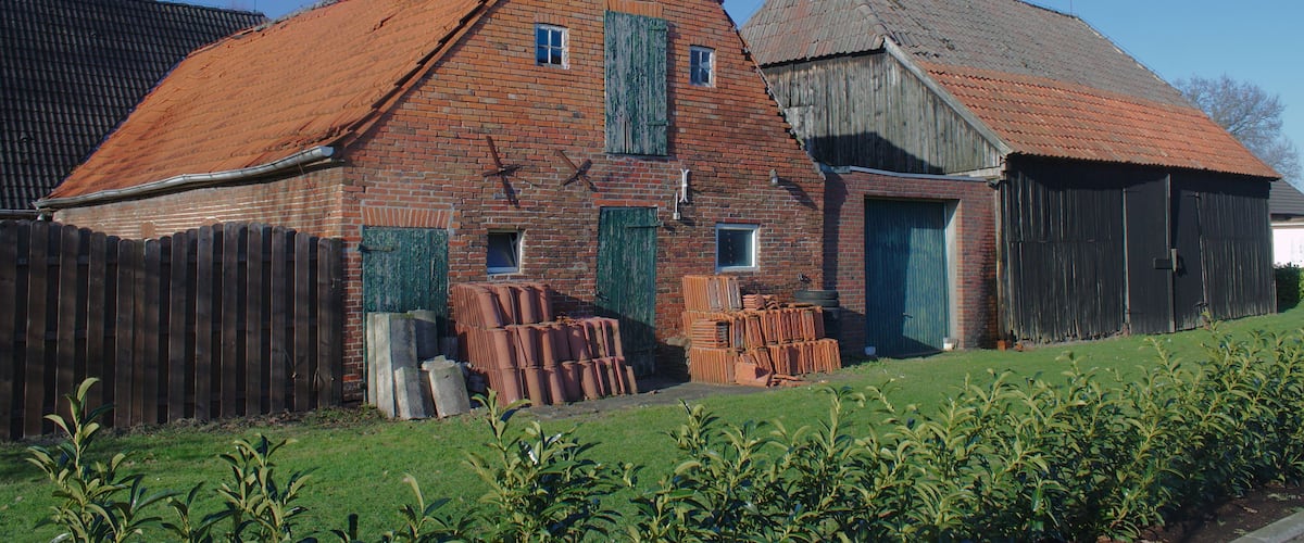 A brick building with a red roof, a wooden barn, and a wooden fence.