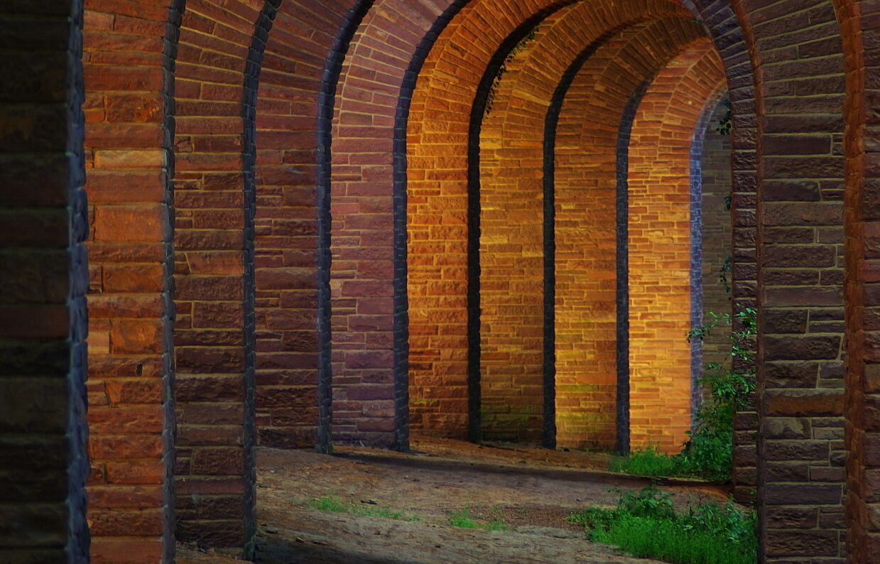 A brick archway with a wooden bench and greenery at the base.