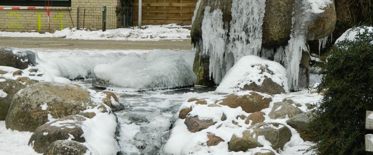 A snow-covered stream with rocks and icicles.