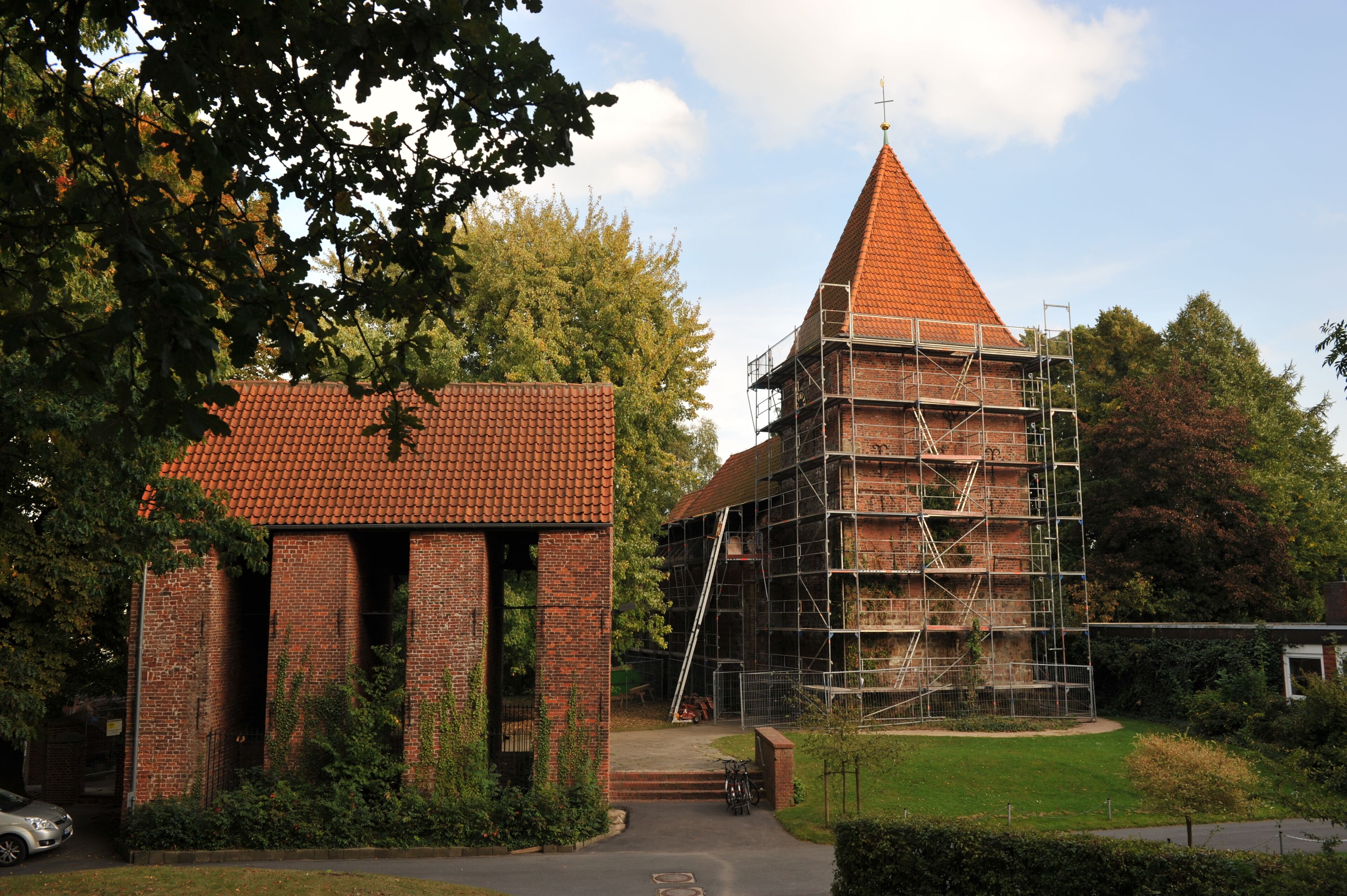 A church with a red roof and a steeple, surrounded by trees and a brick building under construction.