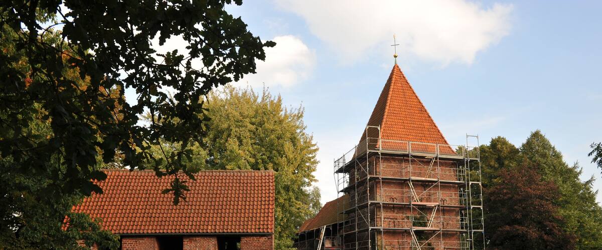 A church with a red roof and a steeple, surrounded by trees and a brick building under construction.