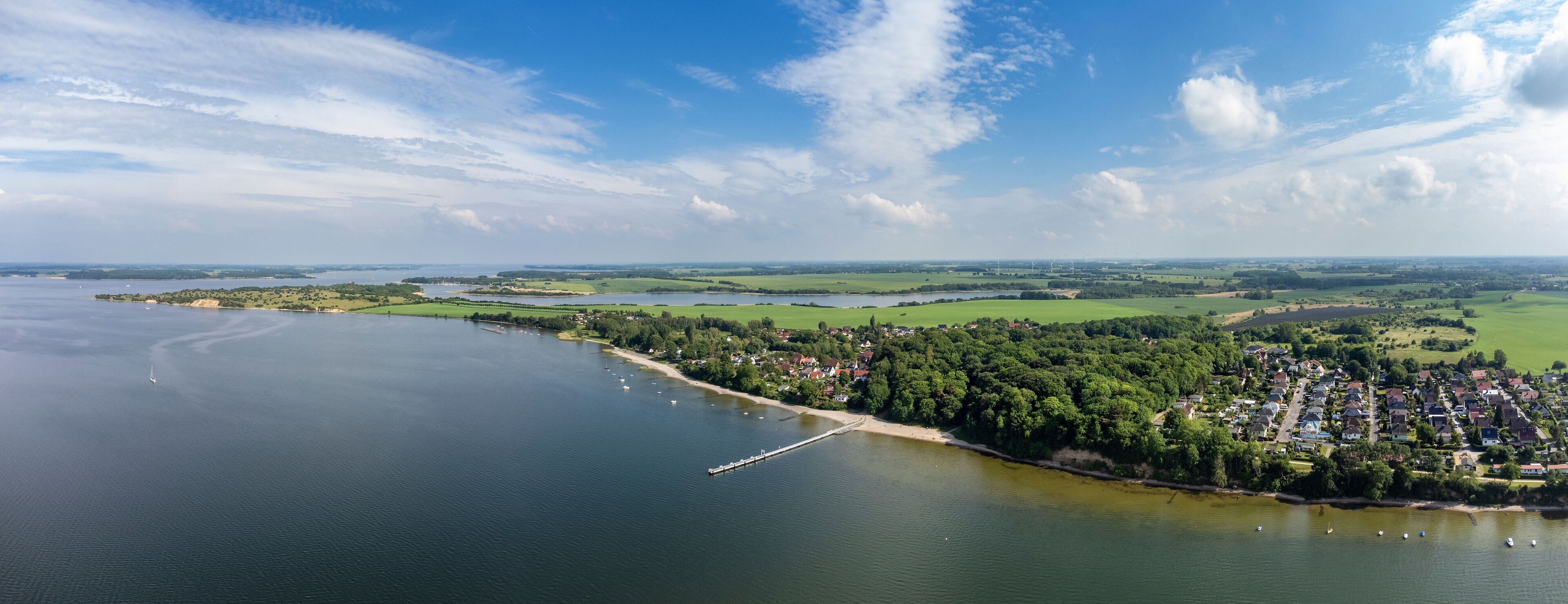 A coastal town with a river, green fields, and wind turbines in the distance.