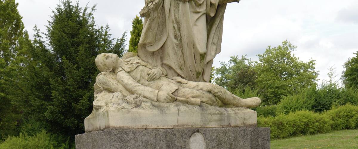 A stone angel statue with a plaque, surrounded by greenery.