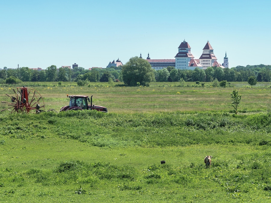 Un campo verde con un tractor y un edificio grande de techo rojo al fondo.