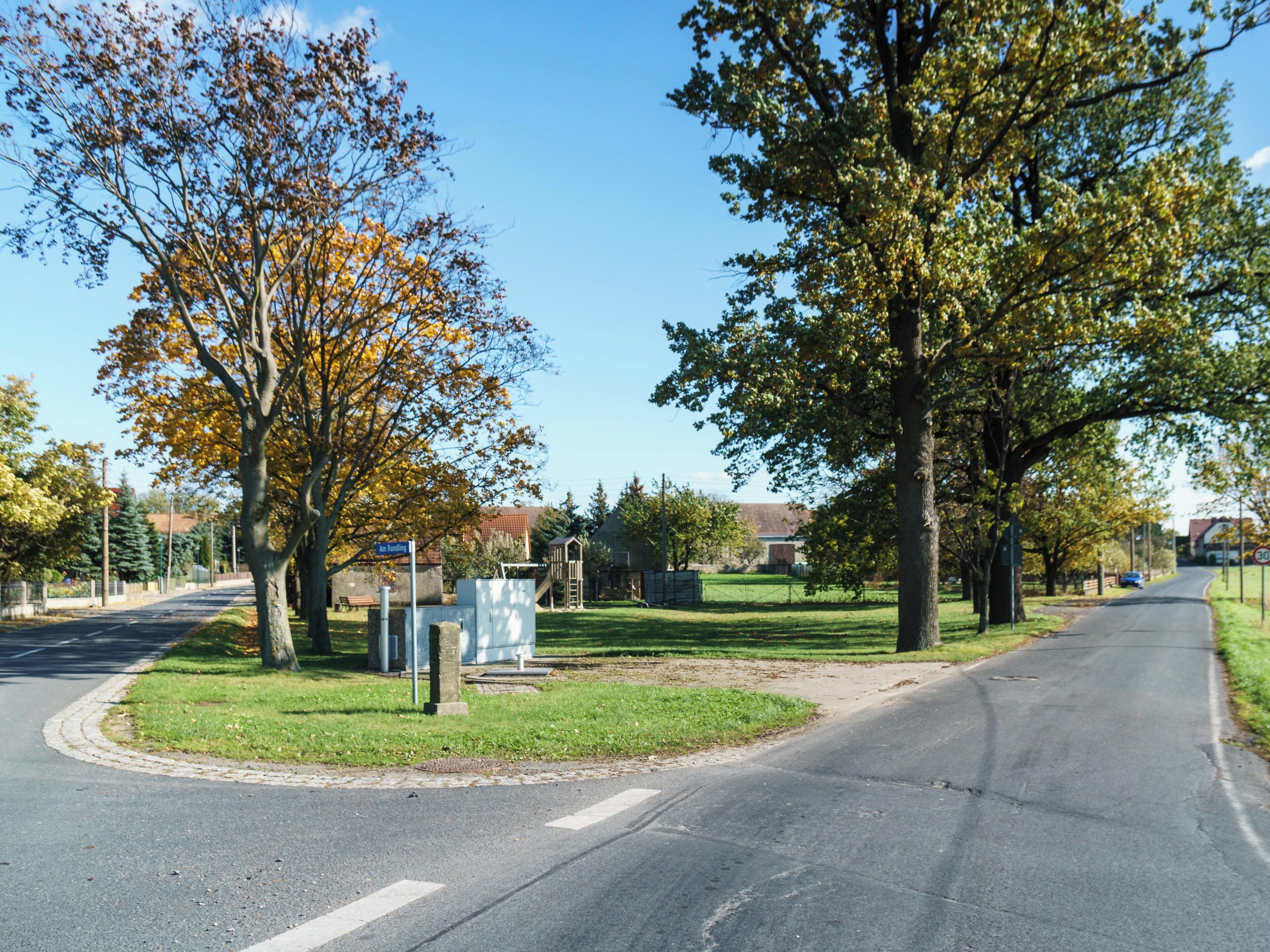 A suburban street lined with trees and a playground.