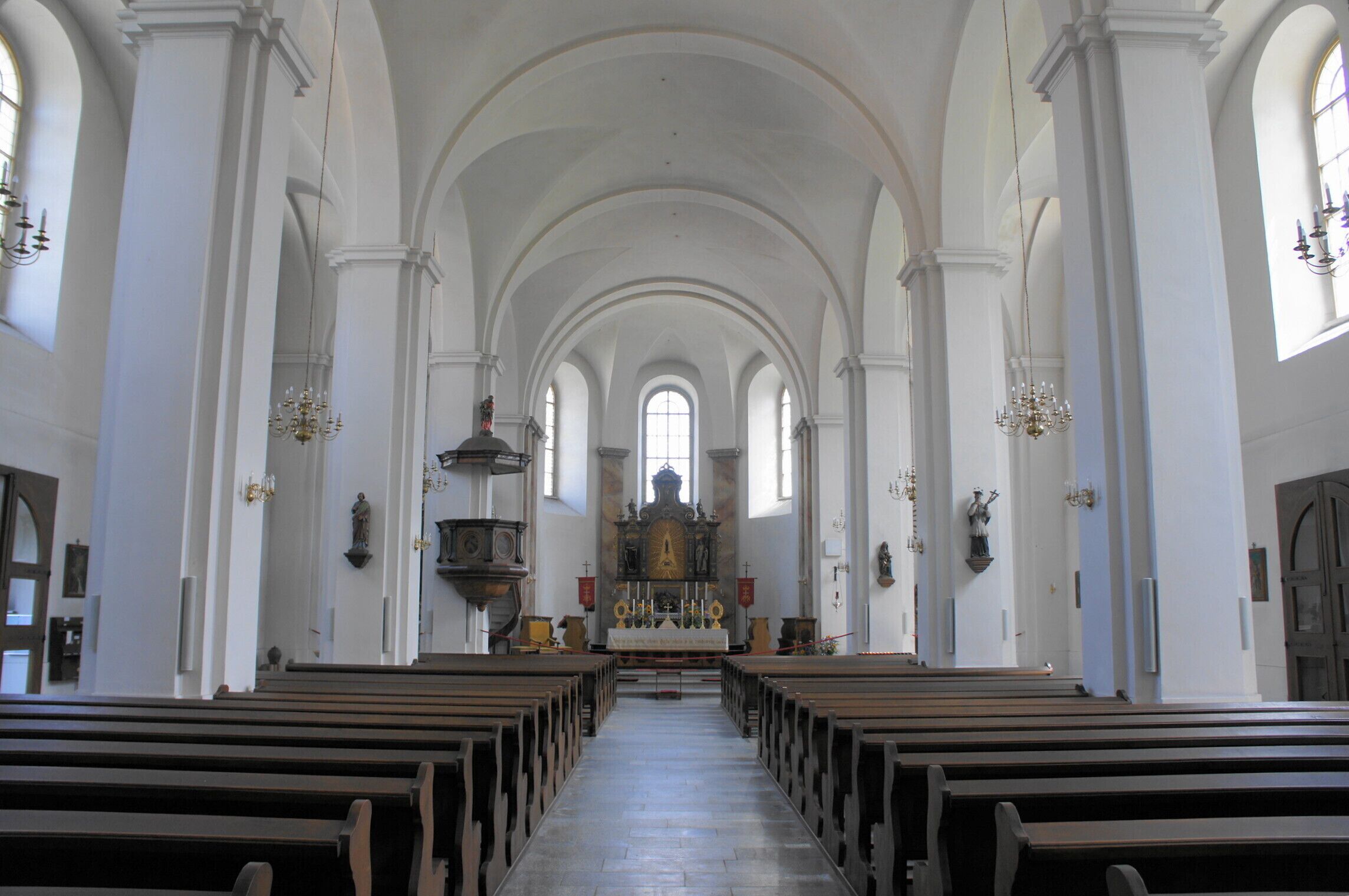 A church interior with arched ceilings, wooden pews, and a central altar.