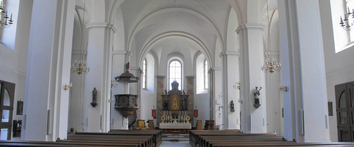 A church interior with arched ceilings, wooden pews, and a central altar.