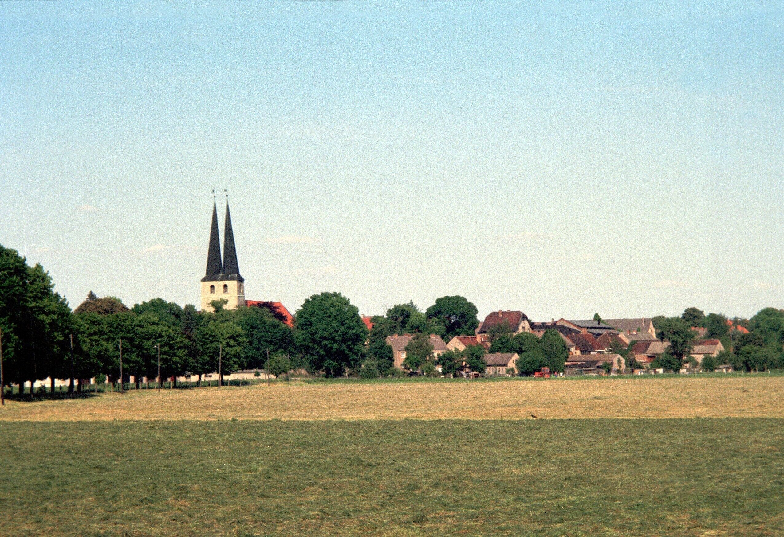 A church with a tall spire, surrounded by trees and houses in a rural setting.