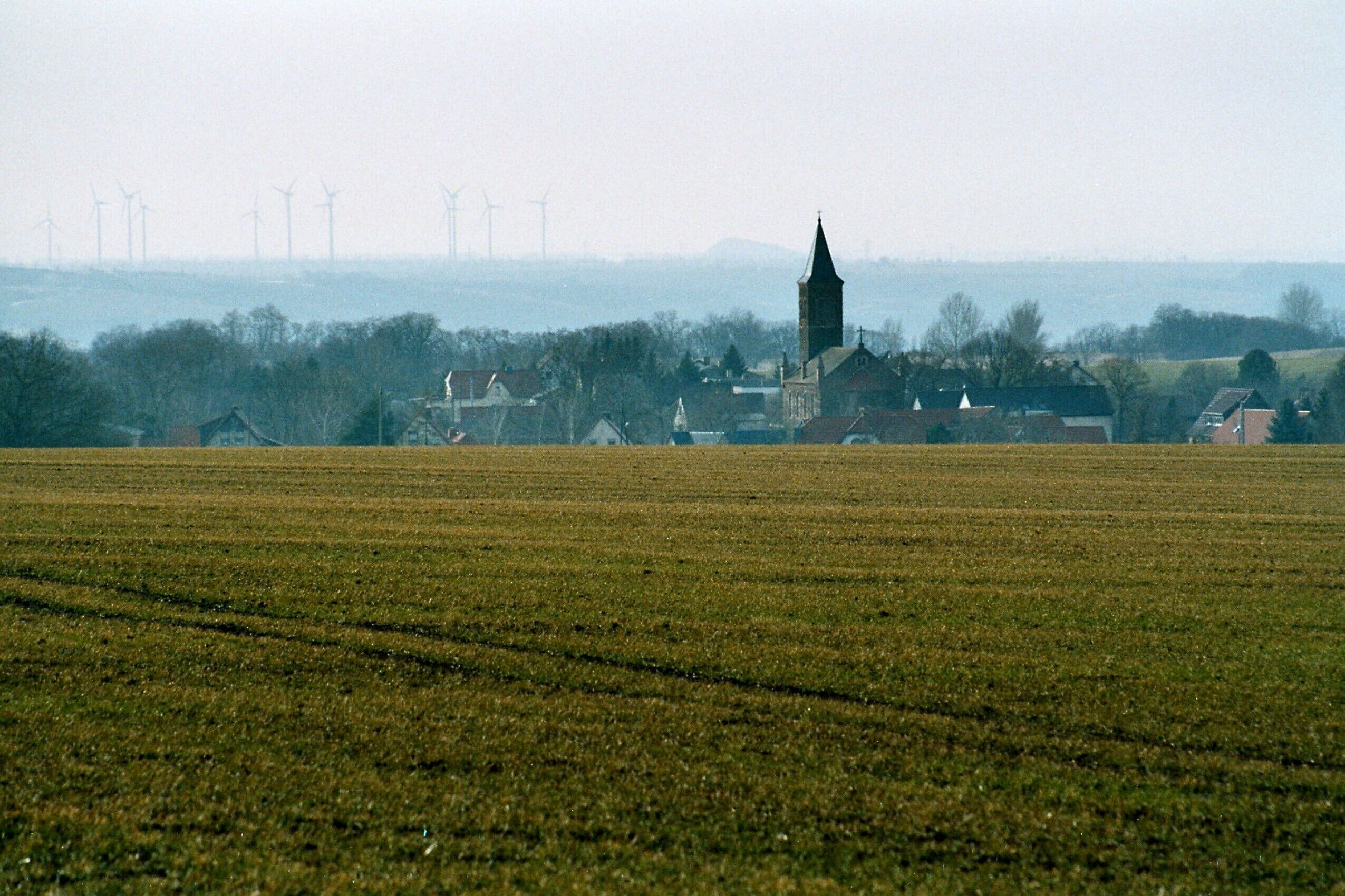 A rural landscape with a church, wind turbines, and a field.